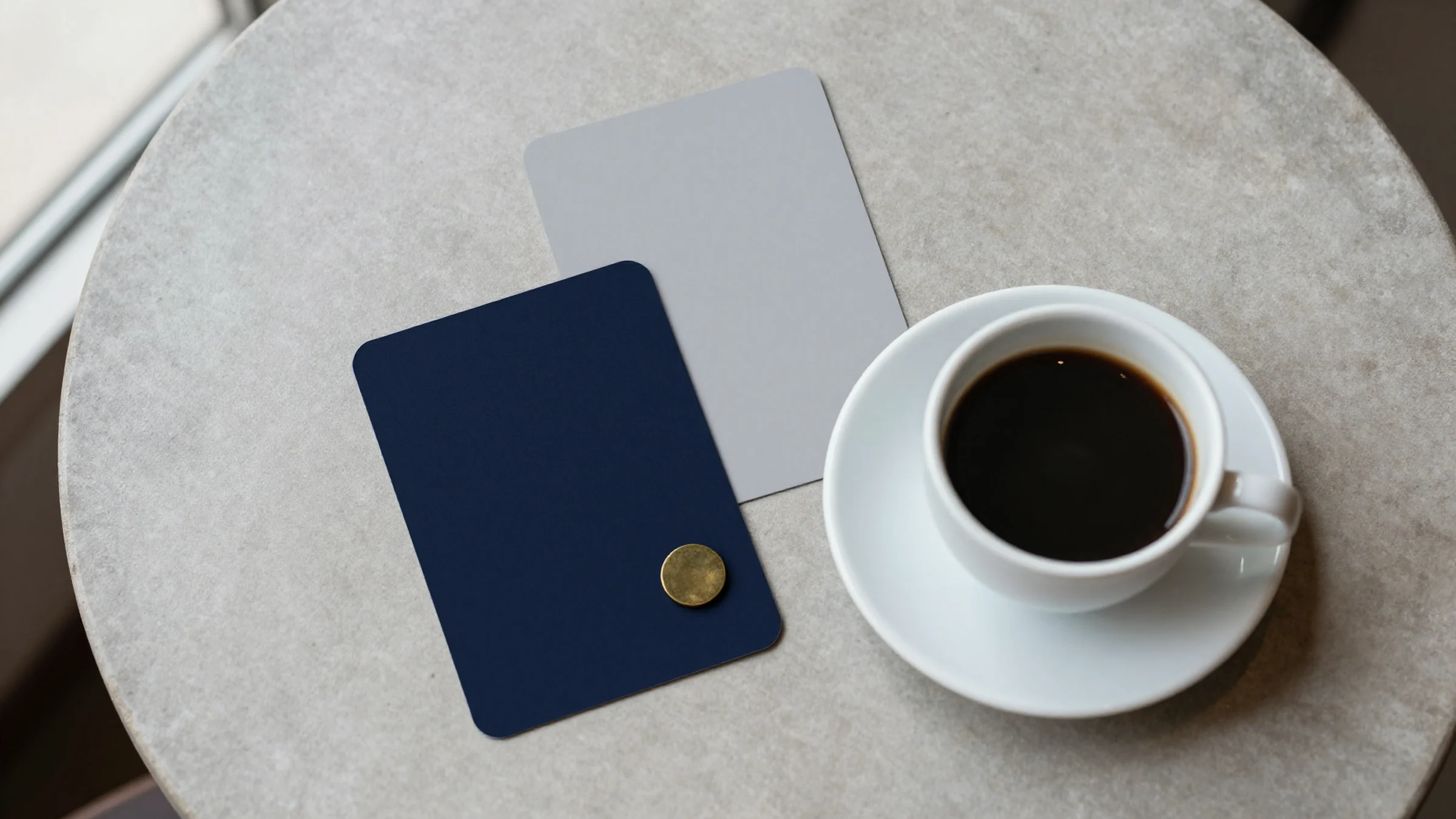 Illustration: two plain cards, one grey and one navy, on a café table, like a question and its answer, with a small brass token on the navy card beside a cup of coffee.